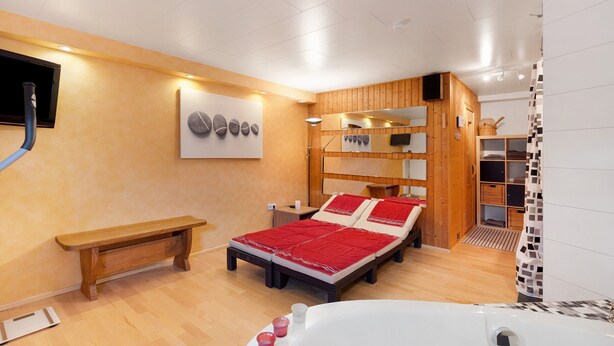 A room with a bed, a bench, a bathtub, and a wooden cabinet.
