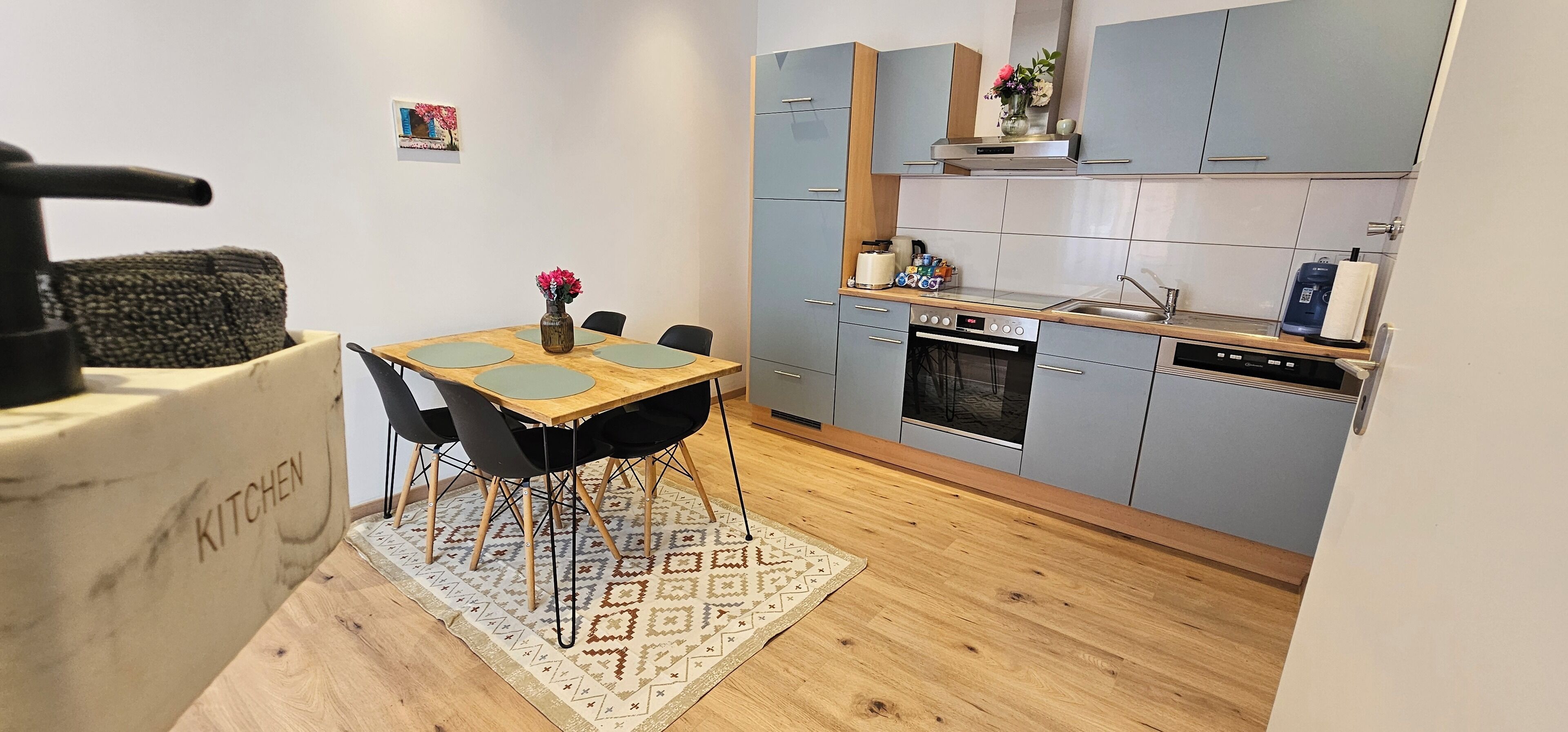 Une cuisine compacte avec des meubles gris, un four encastré et un petit coin repas comprenant une table et des chaises.