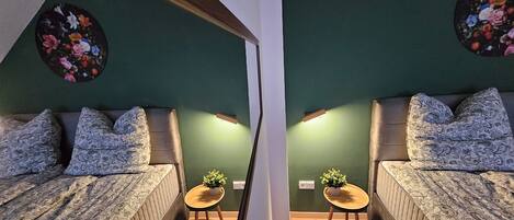 A mirrored room with green walls, two sofas with patterned cushions, and two small tables with potted plants.