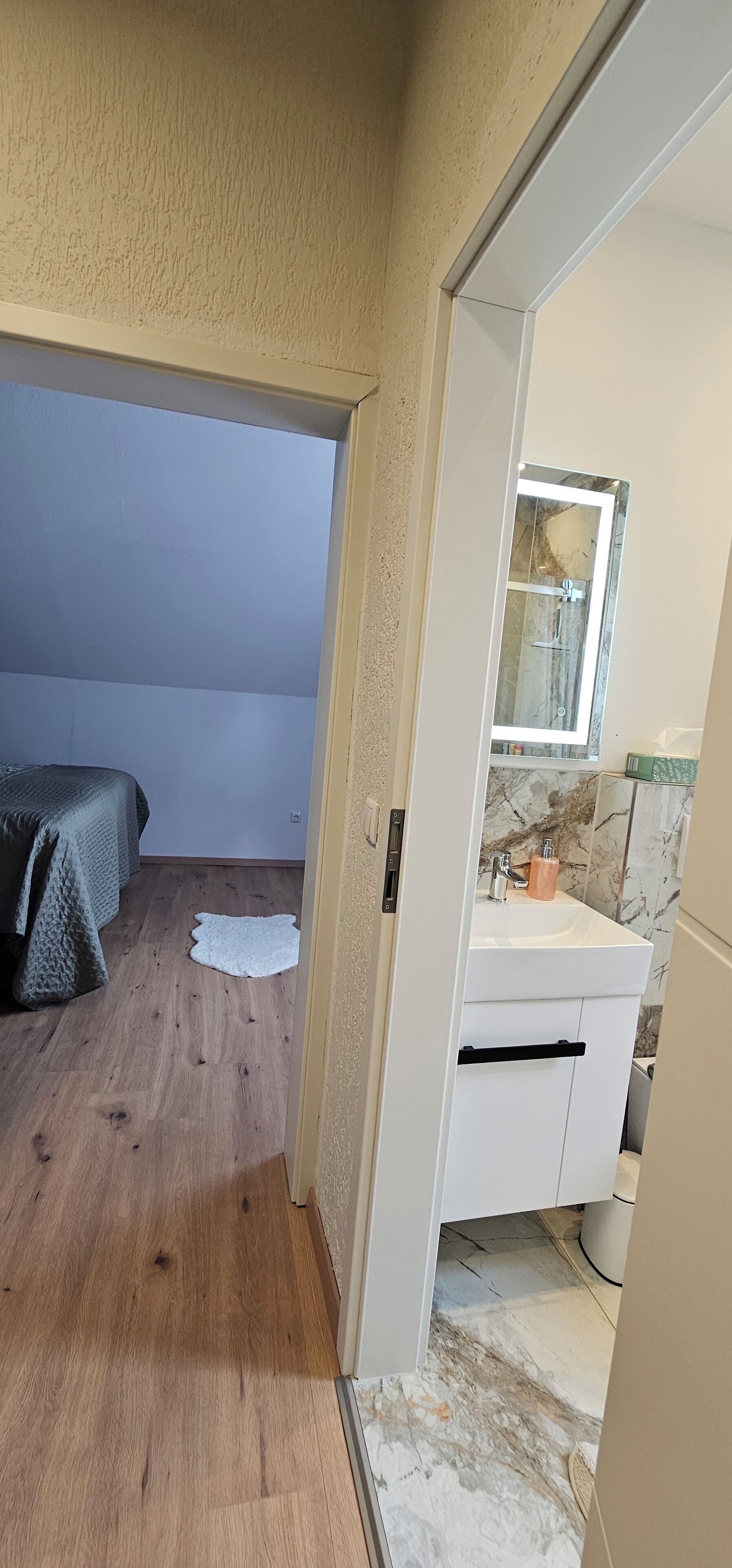A bedroom with a bed, a white rug, and a bathroom with a sink and mirror.