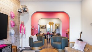 A modern living room with a wooden floor, two grey armchairs, a brown sofa, a wooden coffee table, and a pink accent wall.
