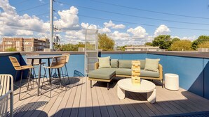 A rooftop deck with a blue pool, outdoor furniture, and a view of the cityscape.