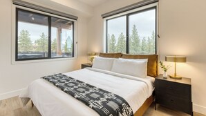 A modern bedroom with a large bed, two bedside tables with lamps, and large windows offering a view of trees. - 2 Units | Minutes to Old Bend, Deck + Hot Tub | 1204 Skyline Ranch by AvantStay (Bend)