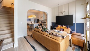 Un salon moderne avec un canapé, une table basse et un téléviseur. Un escalier mène à une autre pièce.