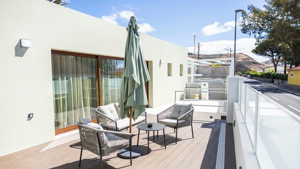 Ein Balkon mit Sitzgelegenheit, eine Schiebetür und Blick auf die umliegende Landschaft.