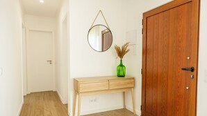 Ein Flur mit Holzboden, einem hölzernen Konsolentisch mit Schubladen, einer grünen Vase mit Trockenpflanzen, einem runden Spiegel an der Wand und einer Holztür.