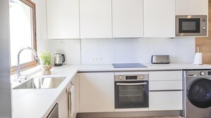Eine moderne Küche mit weißen Schränken, Edelstahlgeräten, einer Spüle, einem Wasserkocher, einem Toaster, einem Backofen und einer Waschmaschine.