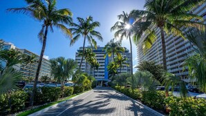 A pathway lined with palm trees leading to a multi-story hotel with balconies.