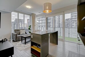 A modern apartment with a living area, kitchenette, and large windows offering city views. - The Skyline Retreat by Instant Suites (Toronto)