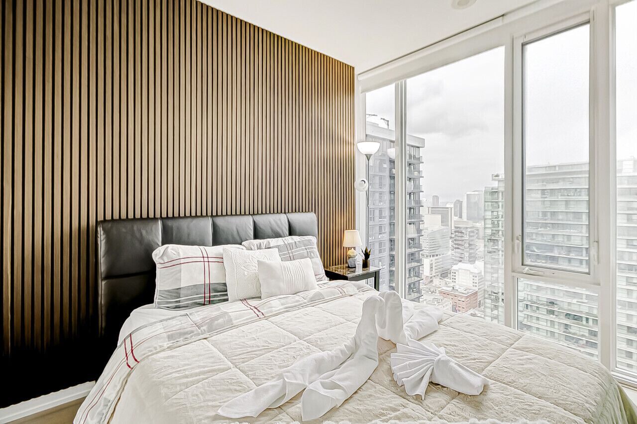 A modern hotel room with a large bed, a wooden panel wall, and a city view.