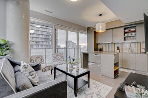 Una sala de estar moderna con un sofá, una mesa de centro y vistas a la ciudad a través de amplios ventanales.