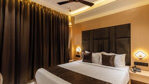 A hotel room with a large bed, dark curtains, a ceiling fan, and bedside lamps. - Hotel Windsor Castle (Mumbai)
