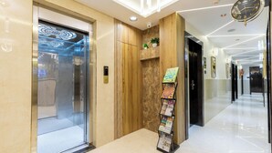A modern hotel lobby with a glass elevator, a reception desk, and a clock on the wall. - Hotel Windsor Castle (Mumbai)