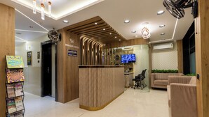 A reception area with a wooden reception desk, a television screen, and a seating area with two sofas. - Hotel Windsor Castle (Mumbai)