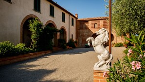 A courtyard with a statue of a horse, a building with arches, and potted plants.