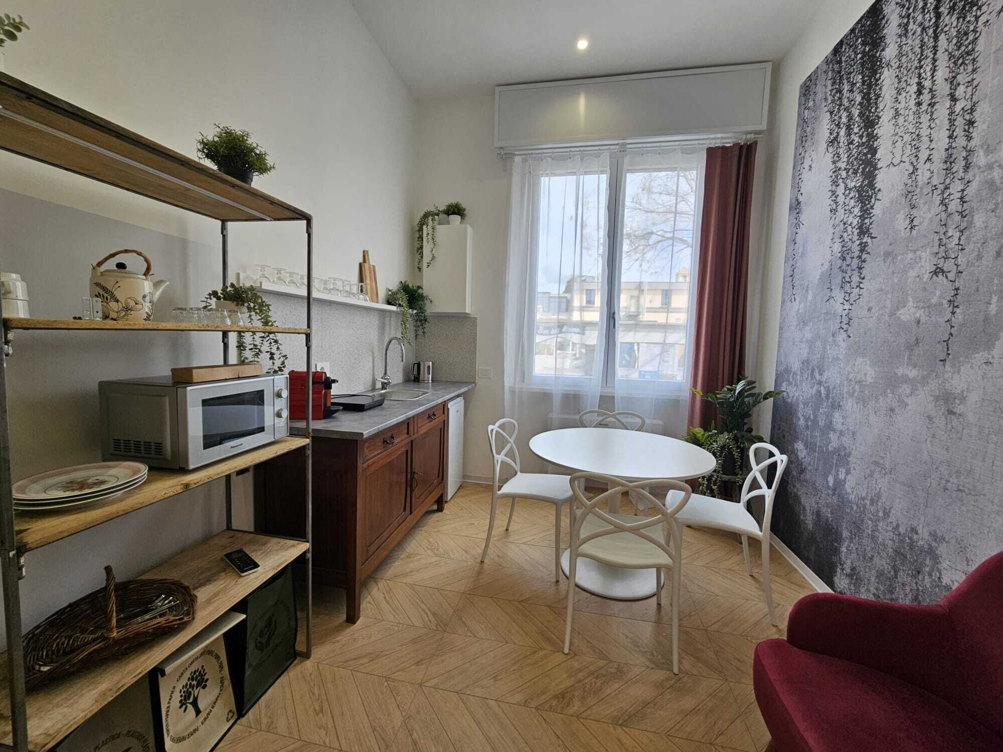 Un espacio habitable compacto con kitchenette, comedor y un amplio ventanal con cortinas.