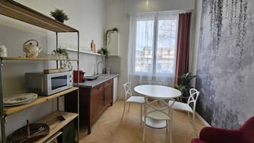 Un espacio habitable compacto con kitchenette, comedor y un amplio ventanal con cortinas.
