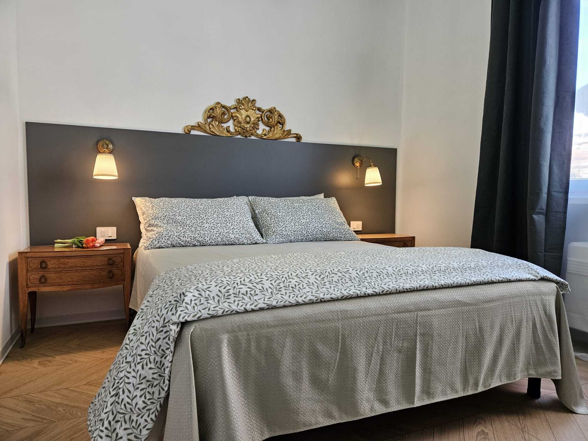 A neatly made bed with patterned bedding, two bedside tables with lamps, and a decorative wall piece above the bed.