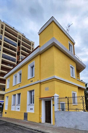 A yellow building with white trim and multiple windows, located next to a taller building.