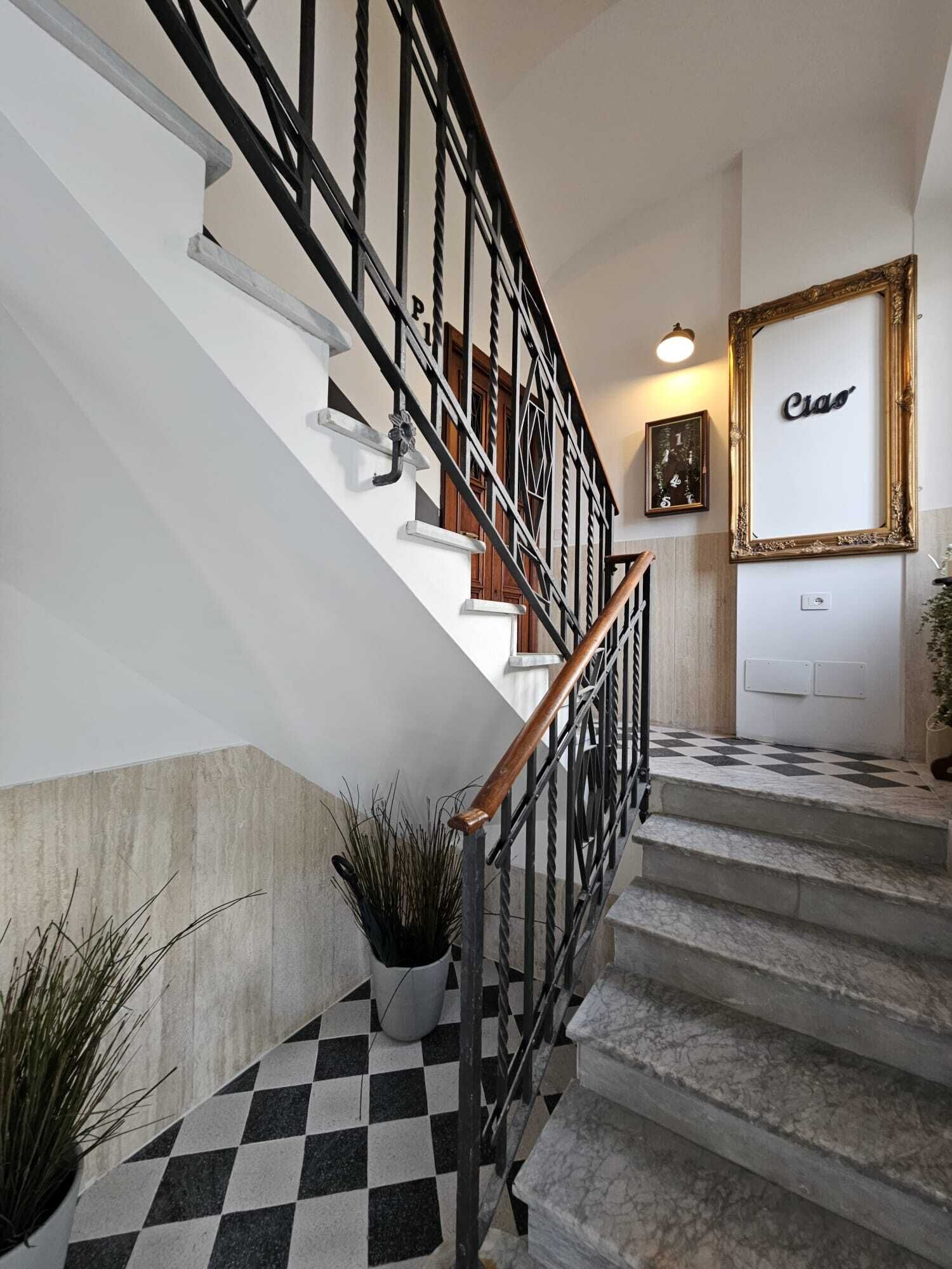 Una escalera con piso blanco y negro a cuadros, barandilla de madera y un letrero en la pared que dice 'Ciao'.