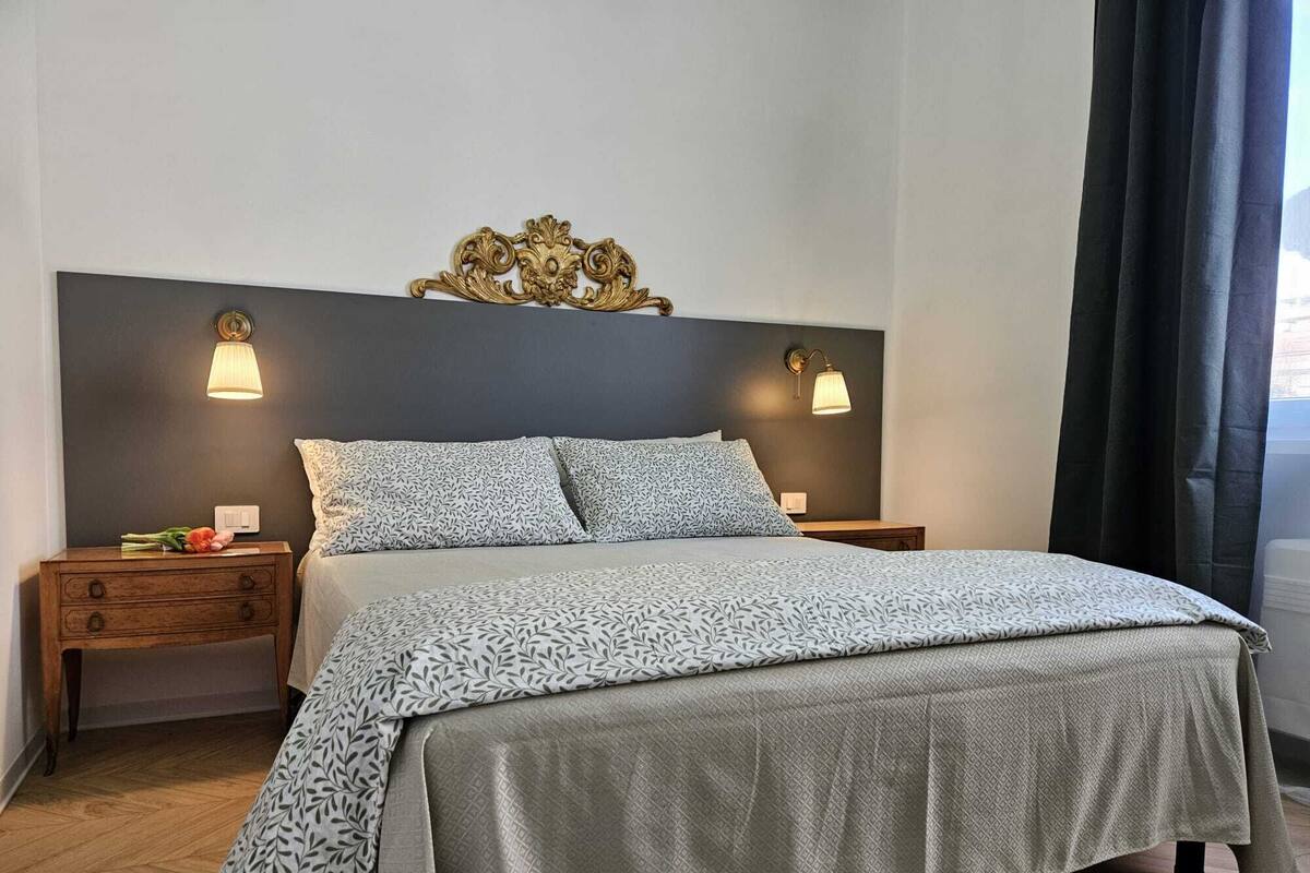 A neatly made bed with patterned bedding, two bedside tables with lamps, and a decorative wall piece above the bed.
