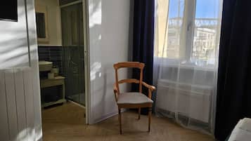 Una habitación con una silla de madera, vista a un edificio a través de una ventana y un baño visible por una puerta abierta.