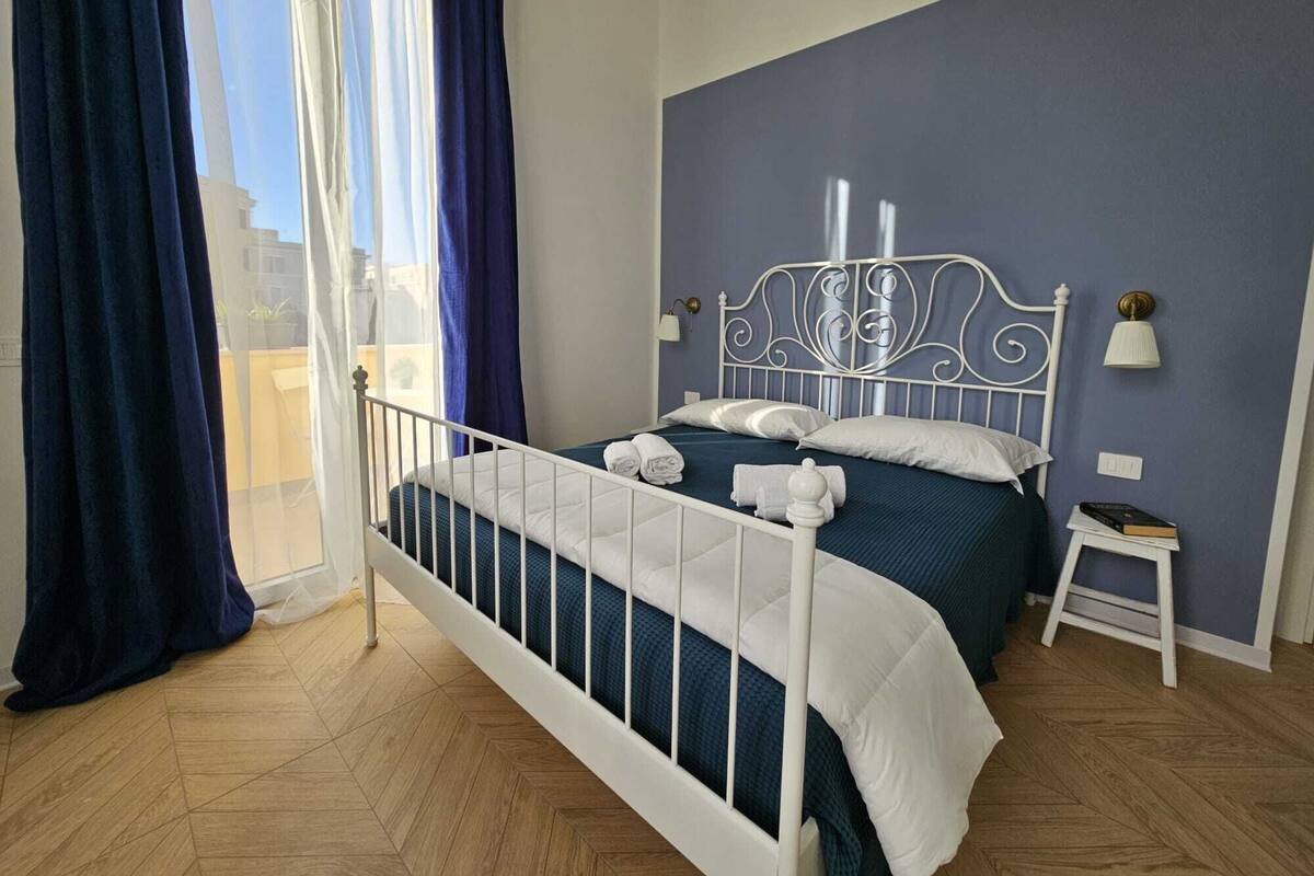A bedroom with a white metal bed frame, a blue wall, and a wooden herringbone floor.