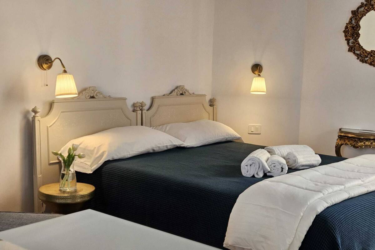A hotel room with two beds, a nightstand with a lamp, and a wall-mounted mirror.
