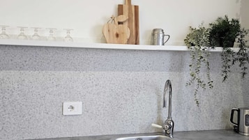 Uma cozinha com bancada de granito, pia de aço inoxidável, tábua de corte de madeira, caneca de metal e um vaso com planta.