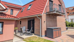 Una casa de dues plantes amb teulada de rajola vermella, un balcó amb barana de metall i una petita zona exterior amb seients i una taula.