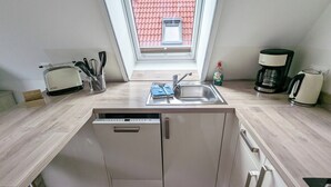 Cuina compacta amb rentaplats, cafetera i torradora. Una finestra ofereix vista a un edifici amb teulada vermella.