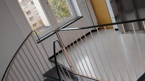 A spiral staircase with metal railings and a view of a building outside through a window. - Kotimaailma Penthouse Studio (Lahti)