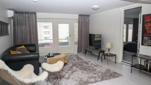 A modern living room with a sofa, a coffee table, a TV, and a rug. - Kotimaailma Penthouse Studio (Lahti)