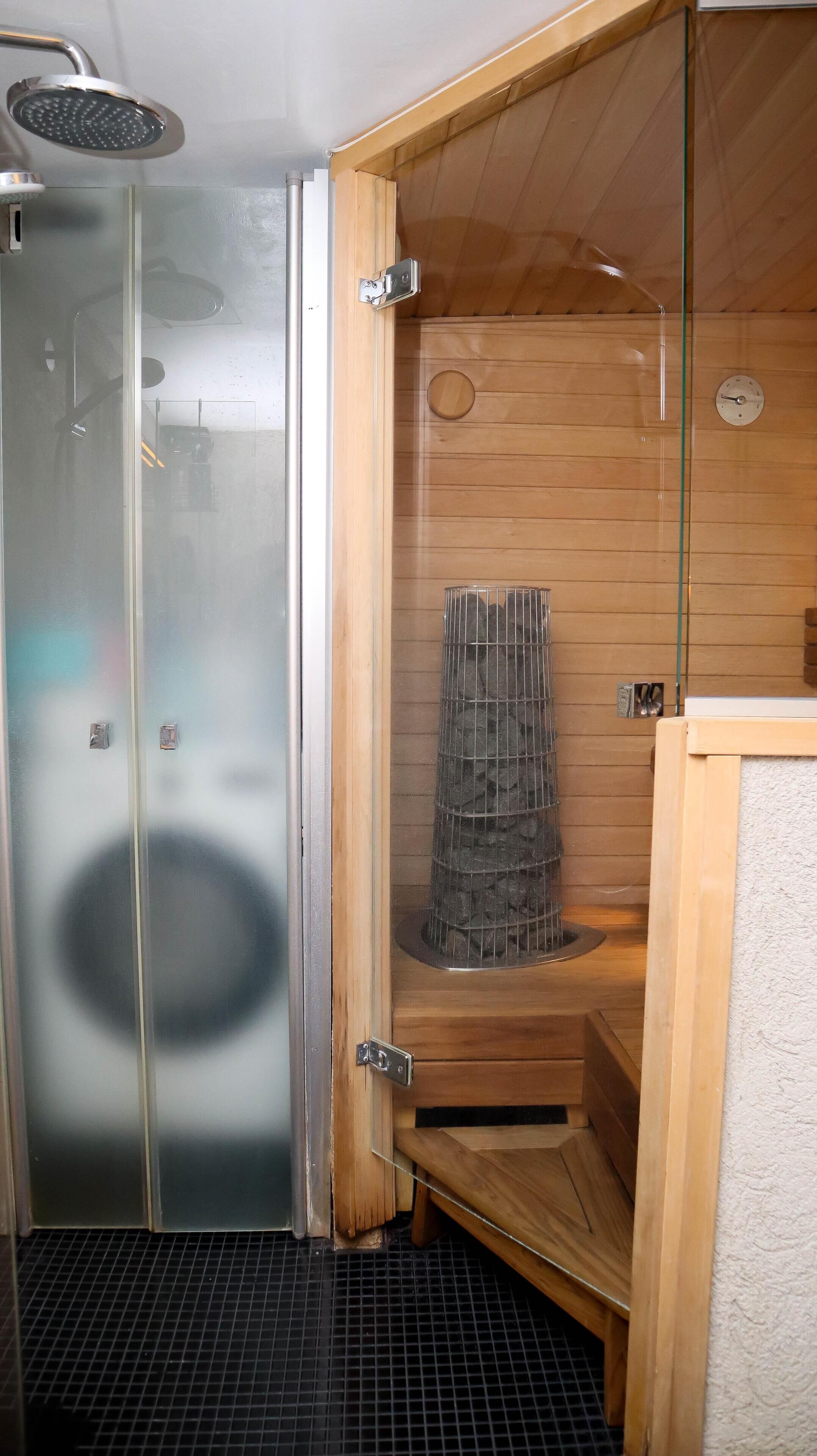 Una sauna con puerta de vidrio, interior de madera y calentador de metal.