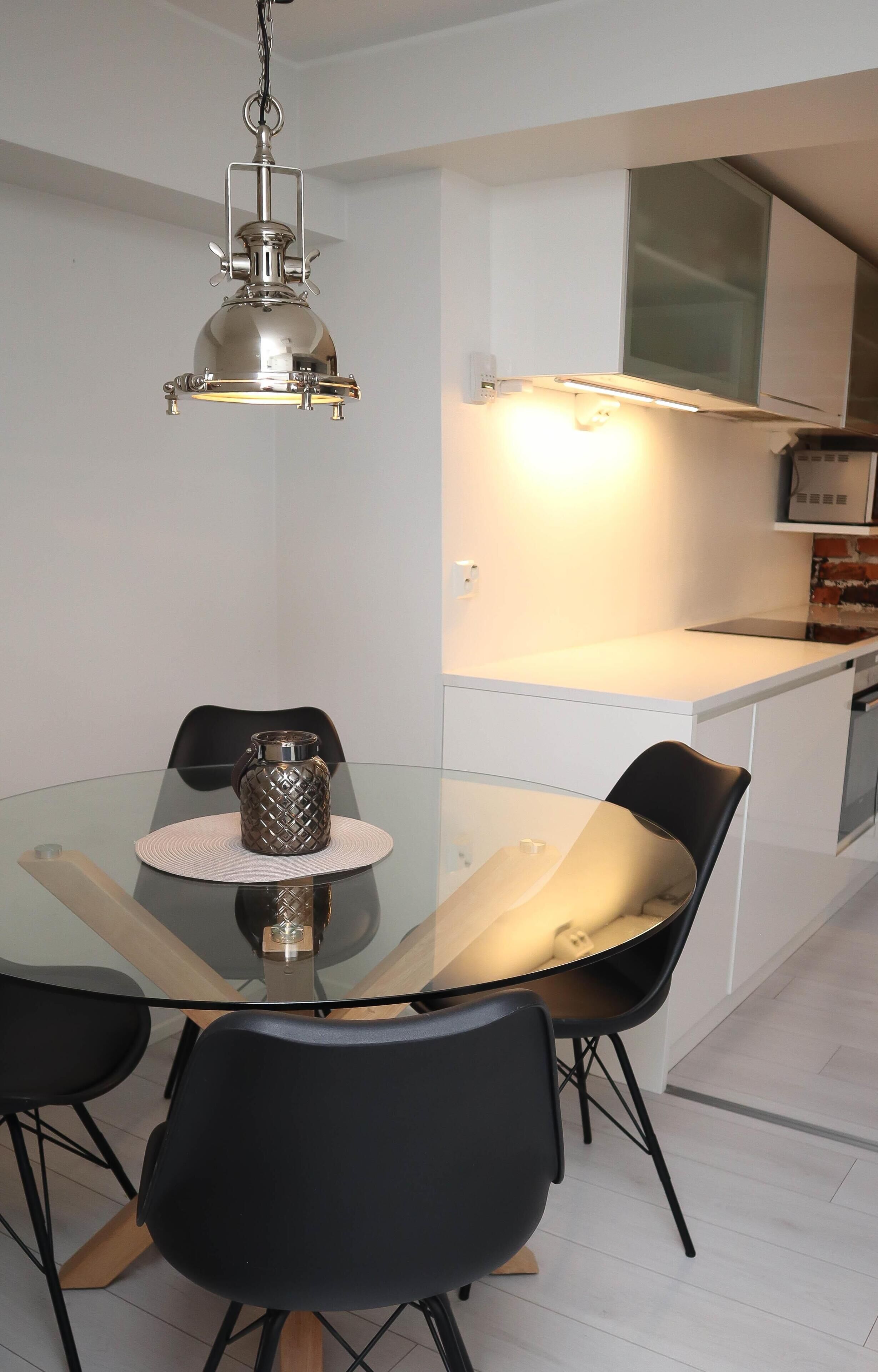 Una cocina moderna con una mesa de comedor de vidrio, sillas negras y una lámpara colgante.