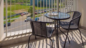A balcony with a table and chairs, offering a view of a parking lot and buildings in the distance.