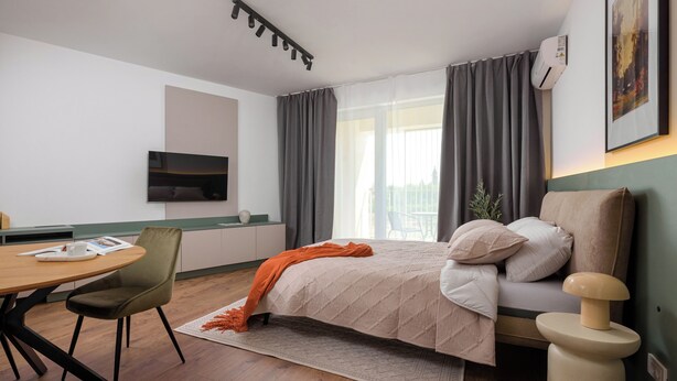 A modern hotel room with a bed, a desk, a chair, and a TV.