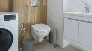 A modern bathroom with a wooden wall, a white toilet, a washing machine, and a sink with a mirror.