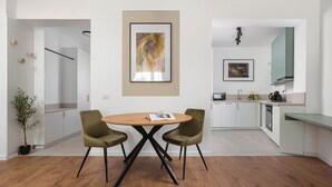 A modern kitchen with white cabinets, a dining area with a round table and two chairs, and a framed abstract painting on the wall.