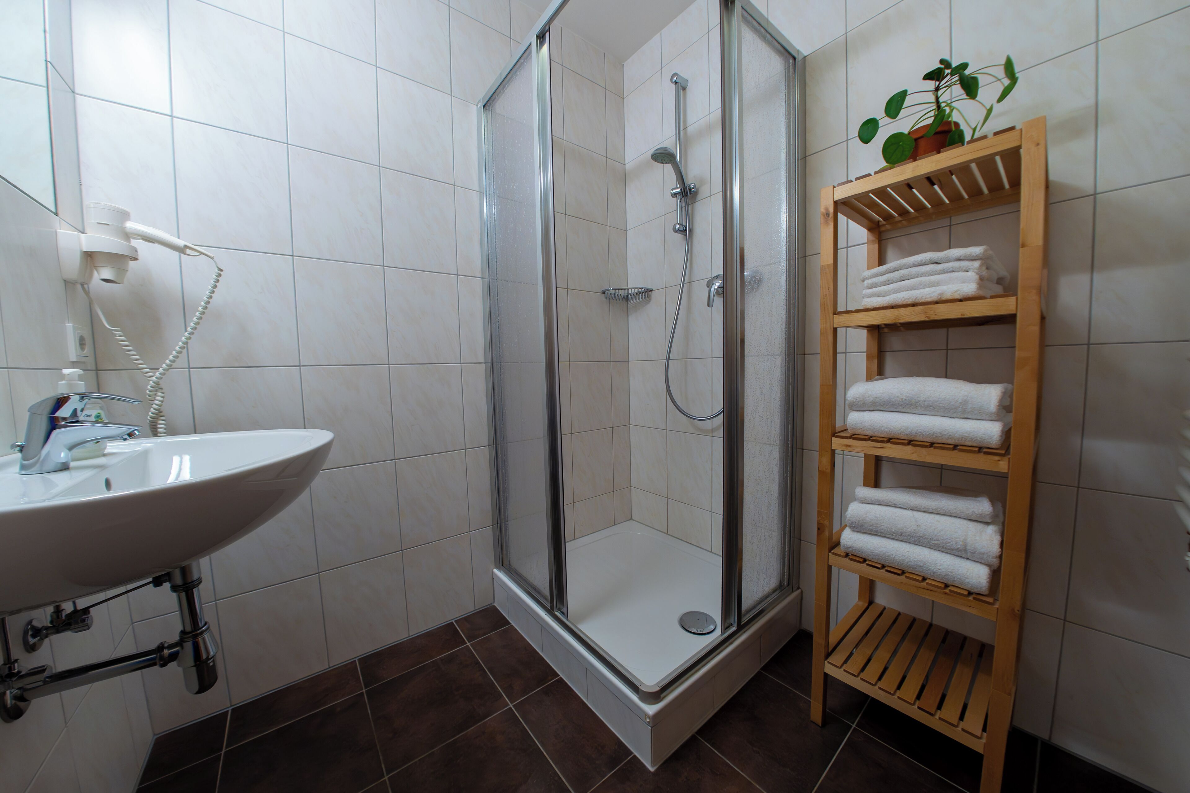 A bathroom with a shower, sink, and a shelf with towels.