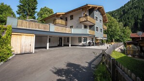 A multi-story hotel with a covered outdoor area, wooden balconies, and a view of a forested hillside. - Appartements MaLo by we rent (Viehhofen)