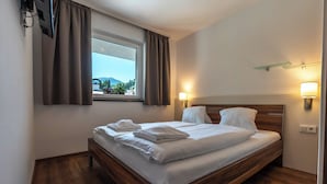 A neatly made bed with white linens and towels, a wooden headboard, a window with curtains, and wall-mounted lights. - Appartements MaLo by we rent (Viehhofen)