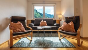 A modern living room with two armchairs, a sofa, and a small coffee table. A large window offers a view of a mountainous landscape. - Appartements MaLo by we rent (Viehhofen)