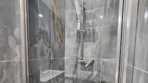 En modern dusch med en glasdörr, ett duschmunstycke som kan hållas i handen och ett duschhandtag.