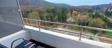 A balcony with a metal railing overlooking a hilly landscape with trees and buildings.