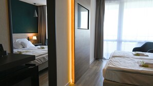 A hotel room with two beds, a desk, a lamp, and a large window with curtains. - Hotel Szieszta (Sopron)