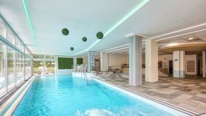 An indoor swimming pool with clear water, surrounded by glass walls and a tiled floor. - Hotel Szieszta (Sopron)