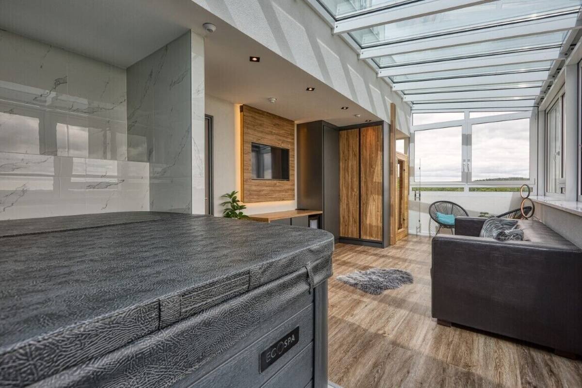 Um spa moderno com teto de vidro, uma mesa de massagem, um banco de madeira e vista para o exterior.