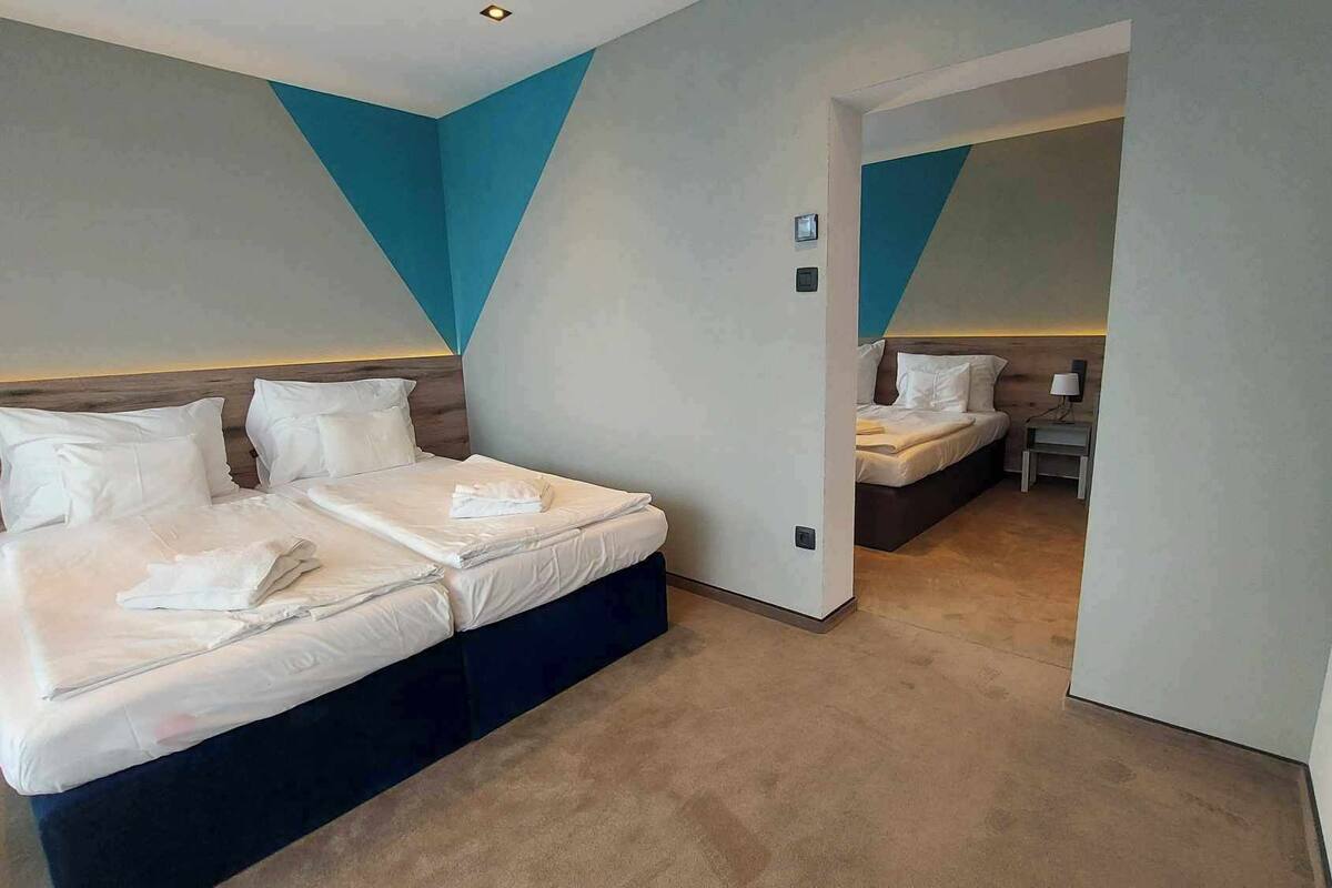 Quarto de hotel moderno com uma cama grande, uma cama menor e um espaço de estar separado.