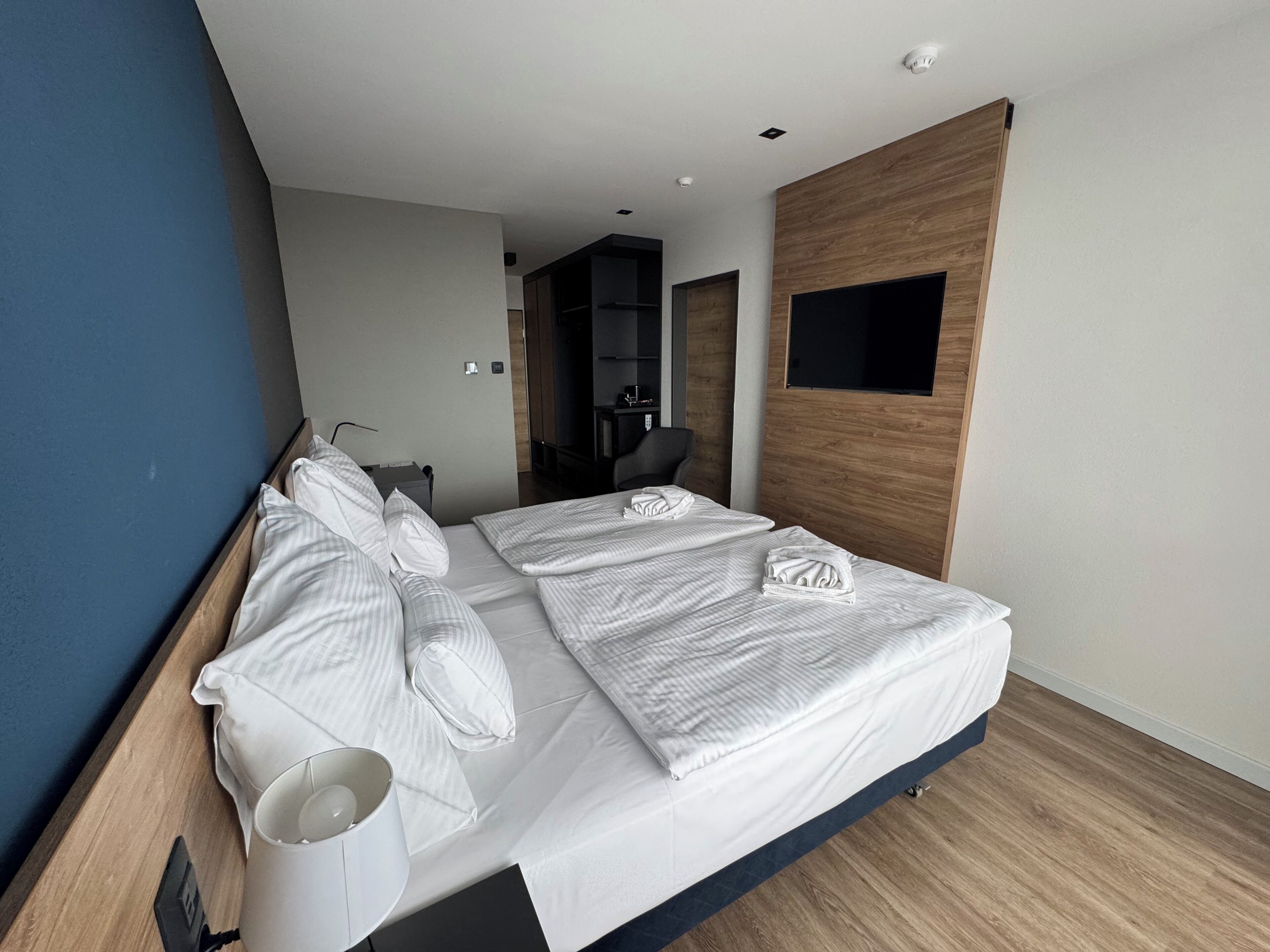 A modern hotel room with a large bed, a desk, and a flat-screen TV mounted on the wall.